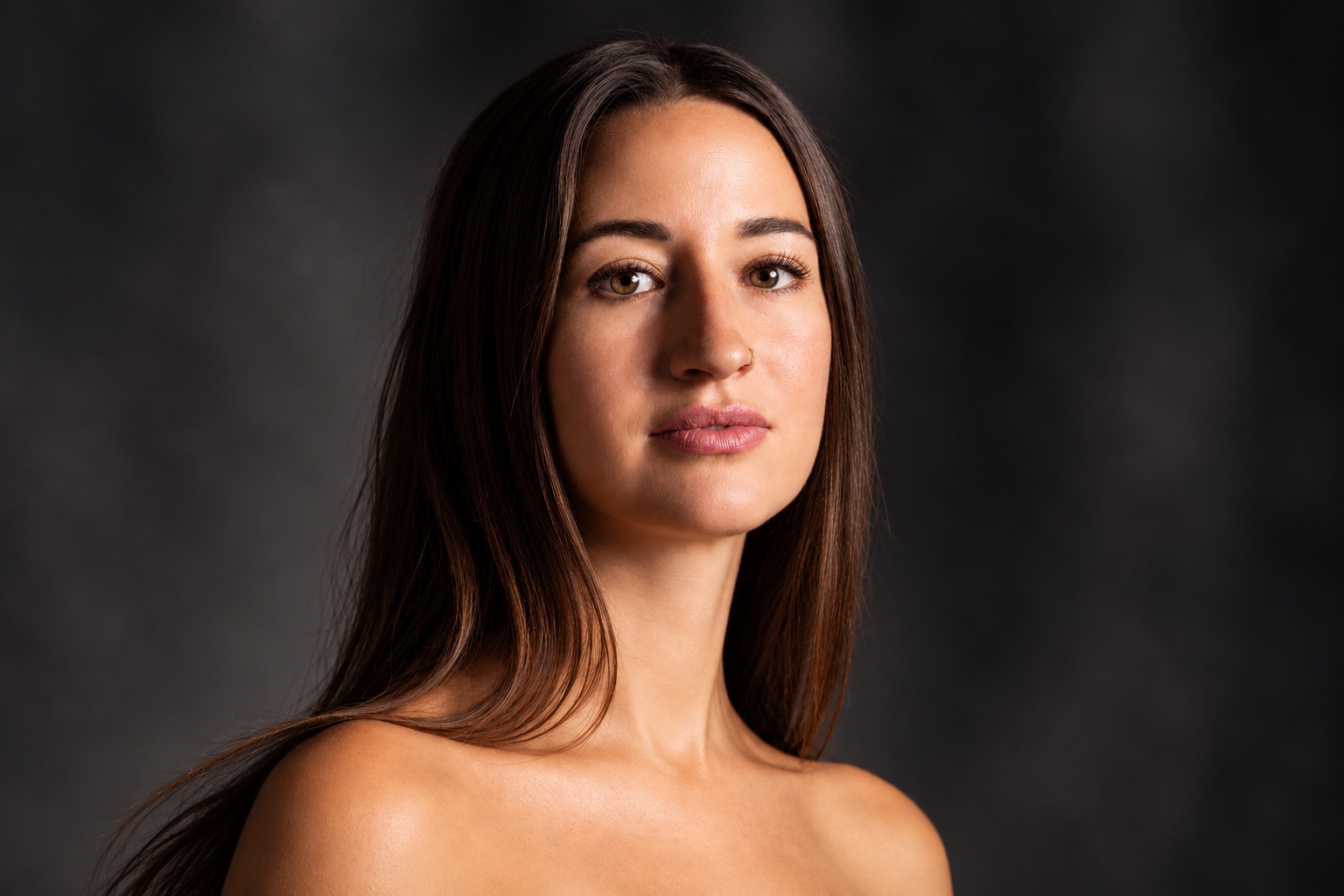 Beauty Portrait einer jungen Frau mit dunklem Haar und ruhigem direkten Blick vor dunklem Hintergrund