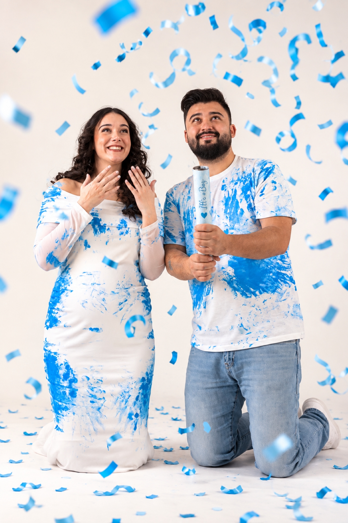 Schwangeres Paar feiert beim Gender-Reveal-Shooting mit blauem Konfetti im Fotostudio.