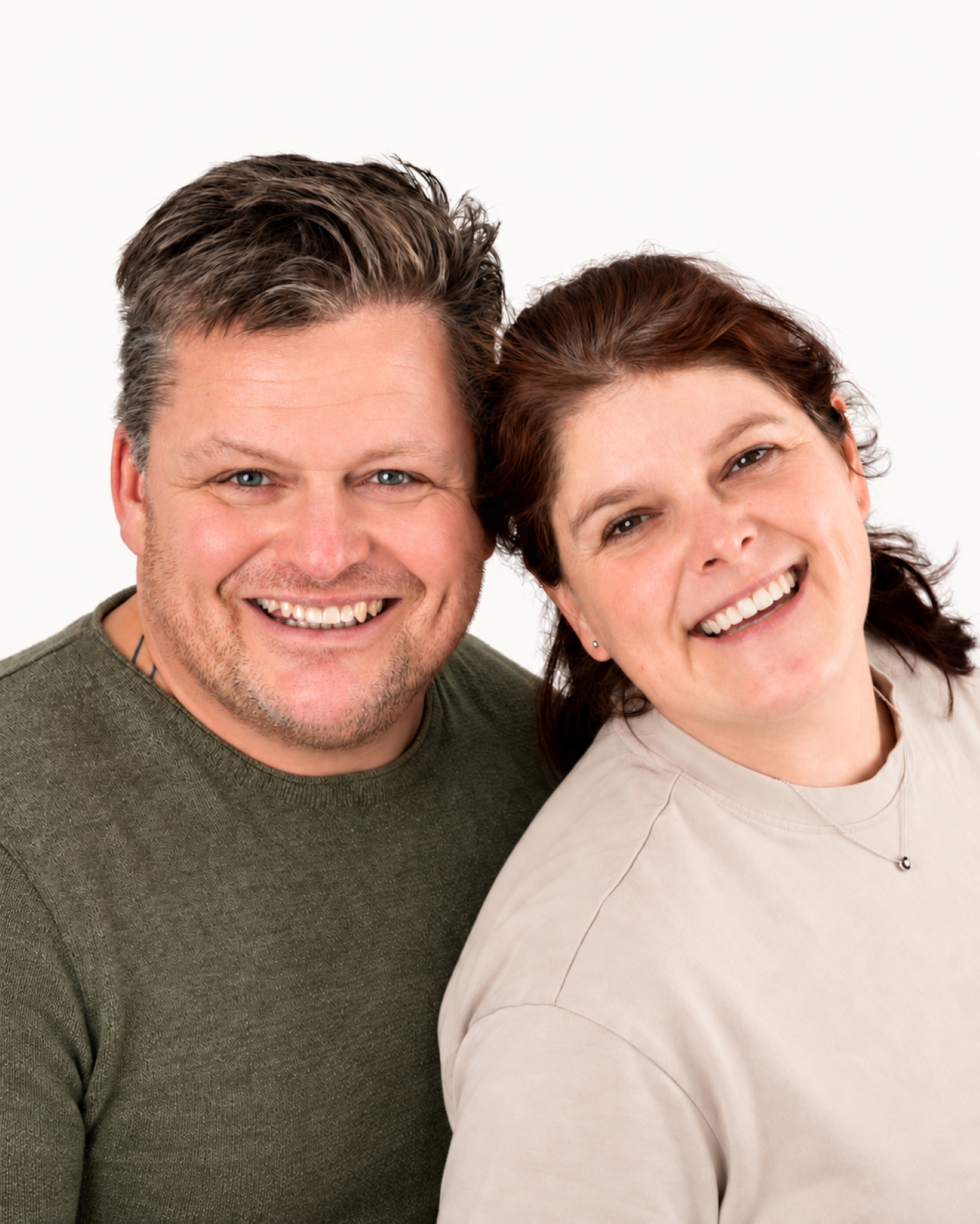 Kathrin und Markus stehen nah beieinander und lächeln in die Kamera vor einem hellen Hintergrund.